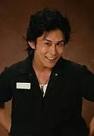 高山猛久(劉鵬)/バストアップ・黒シャツ・両手腰・ネックレス・背景茶色・微笑/舞台｢風魔の小次郎｣